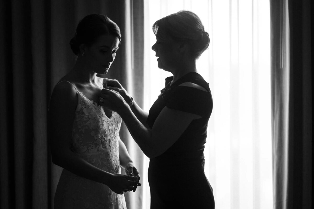 A timeless black and white image of a mother helping her daughter, the bride, into her wedding dress
