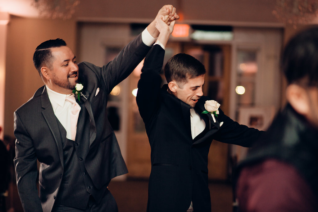 Wedding Photograph Of Groom And Man In Gray Suit Raising Their Hands While Dancing Los Angeles