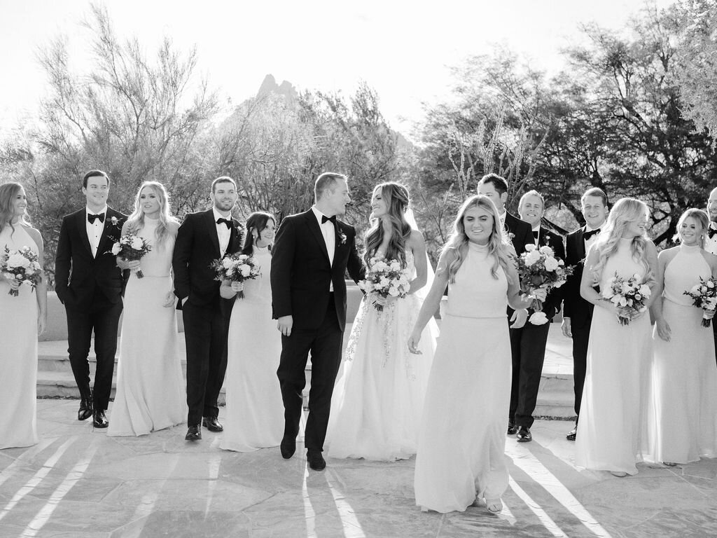 A joyful bridal party walks together, celebrating love and friendship in an elegant outdoor wedding setting. Capturing the beauty of timeless wedding moments.
