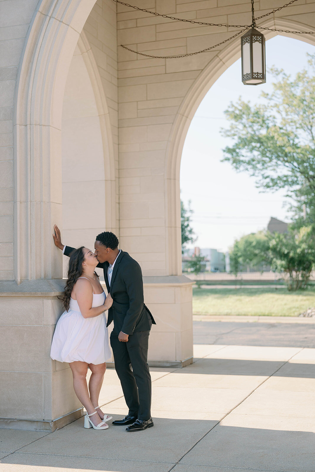 Romantic kiss under stone arch during downtown Kalamazoo engagement session.