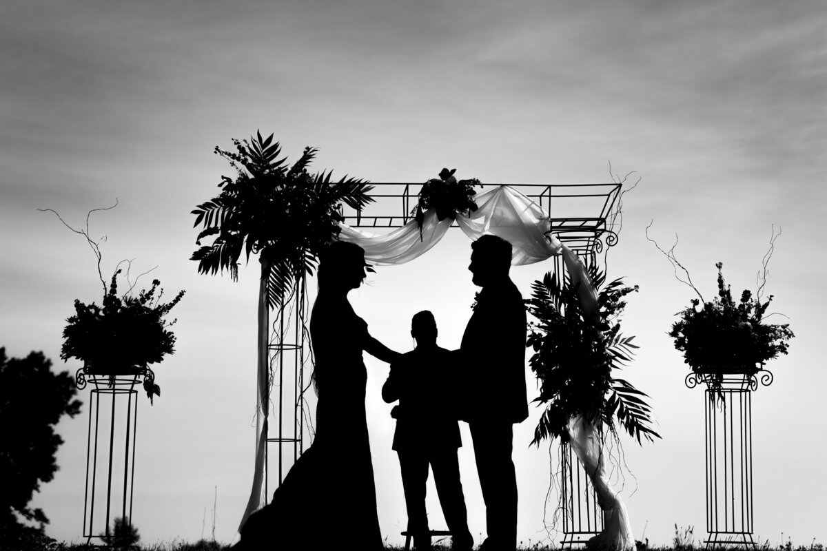 Silhouette of a bride, groom, and their officiant under an arch at a backyard wedding in Galloway, Ohio.