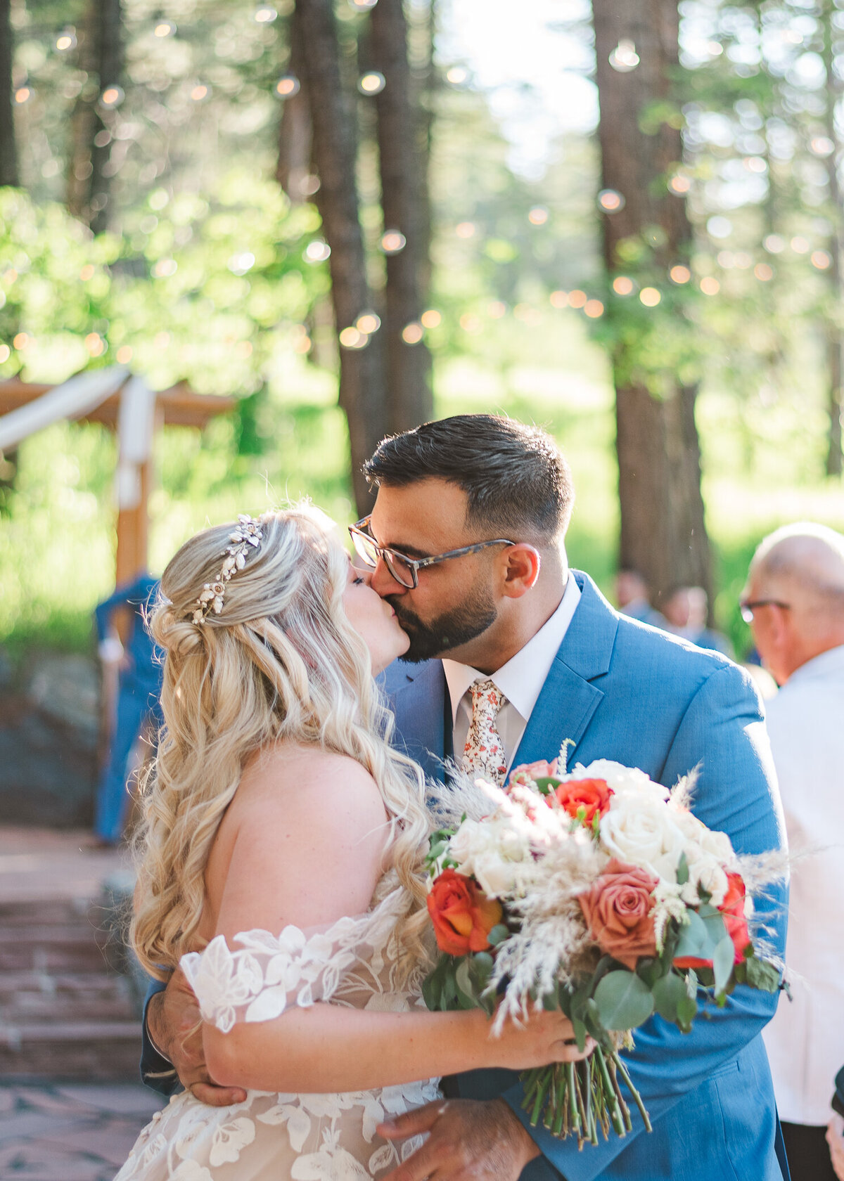 Denver wedding photographer captures bride and groom kissing as they exit their ceremony. Bride has a bouquet of white and red flowers