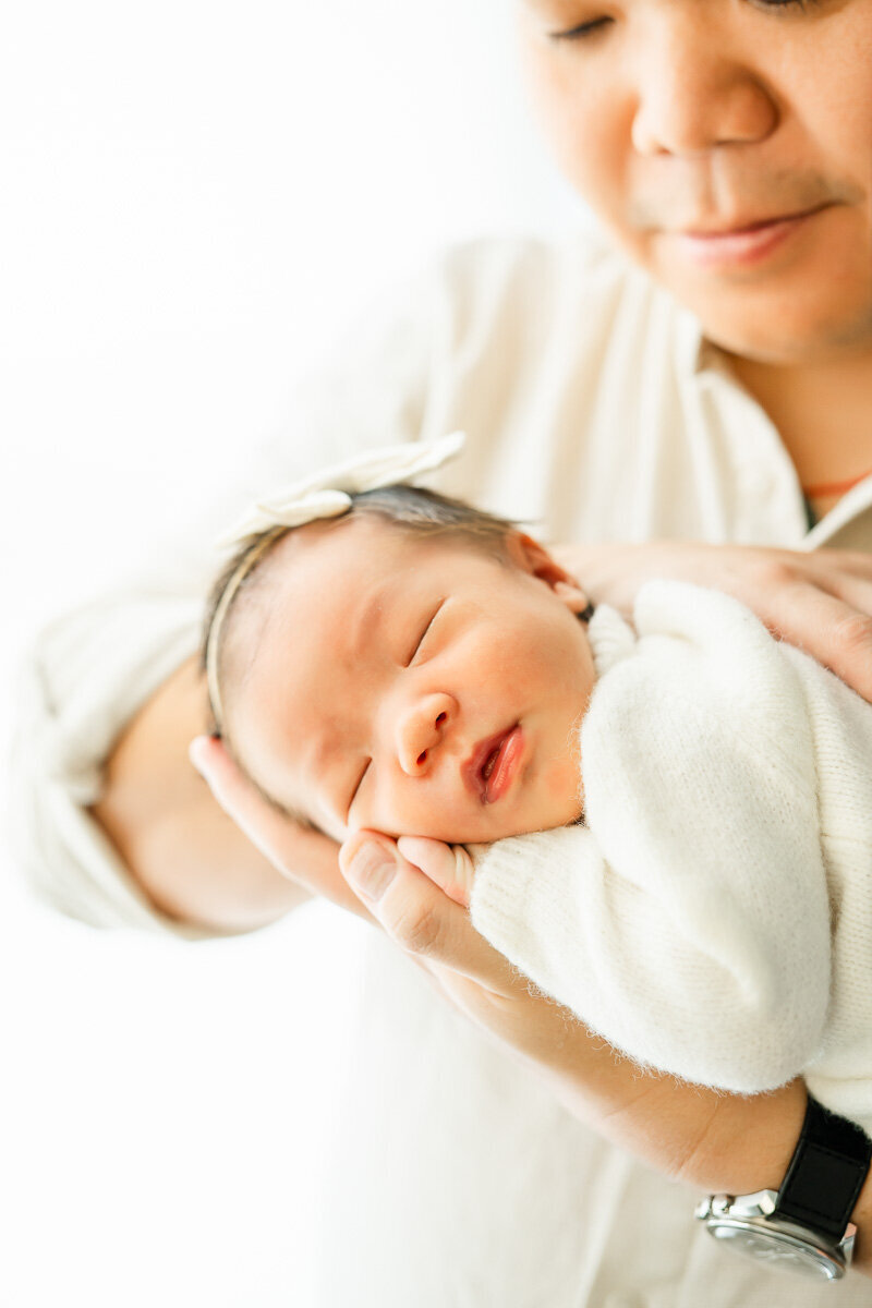 a newborn girl rests her head in her father's hand during their lifestyle session in their Austin home.