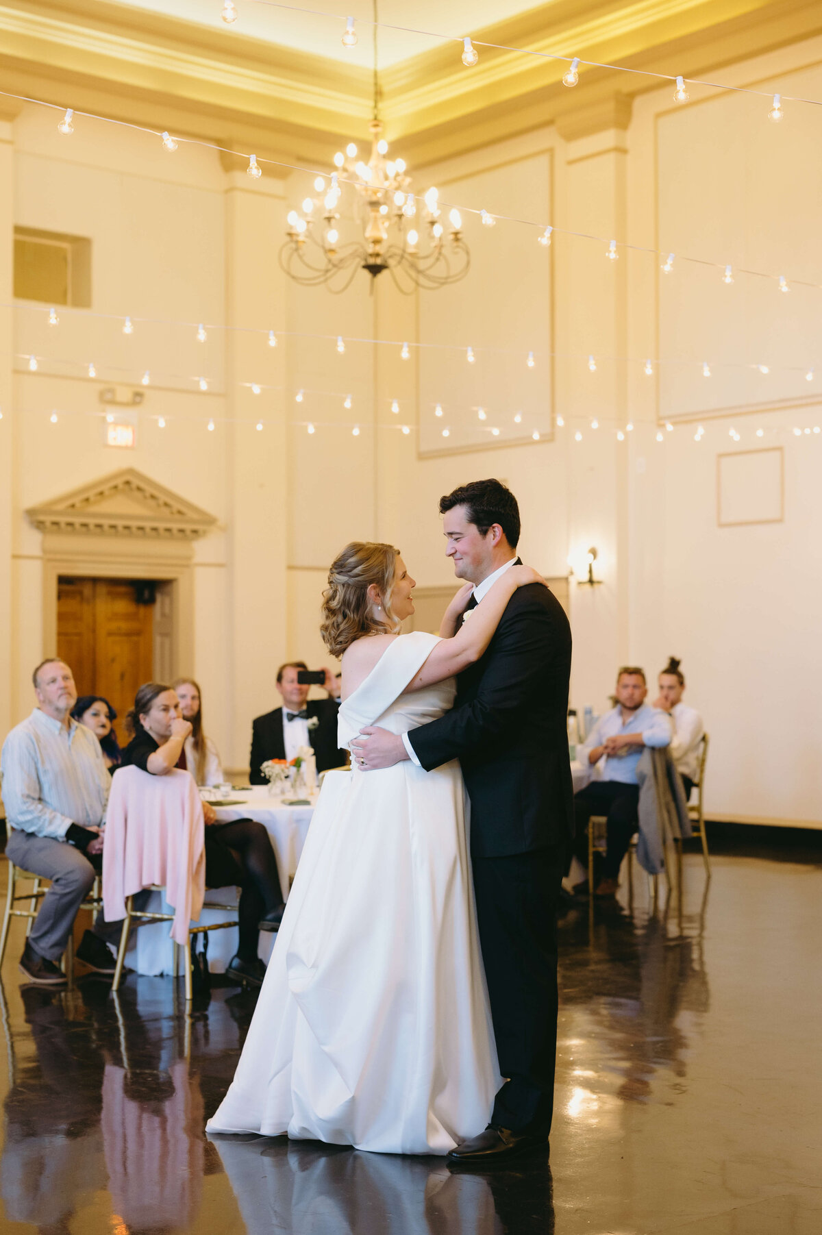 richmond weddings with indoor reception with first dance between the bride and groom  in a grand hall with wedding guests in gold chairs watching the dance