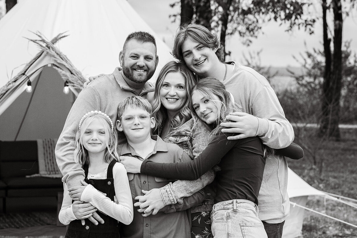 family of six with heads together and yurt in background