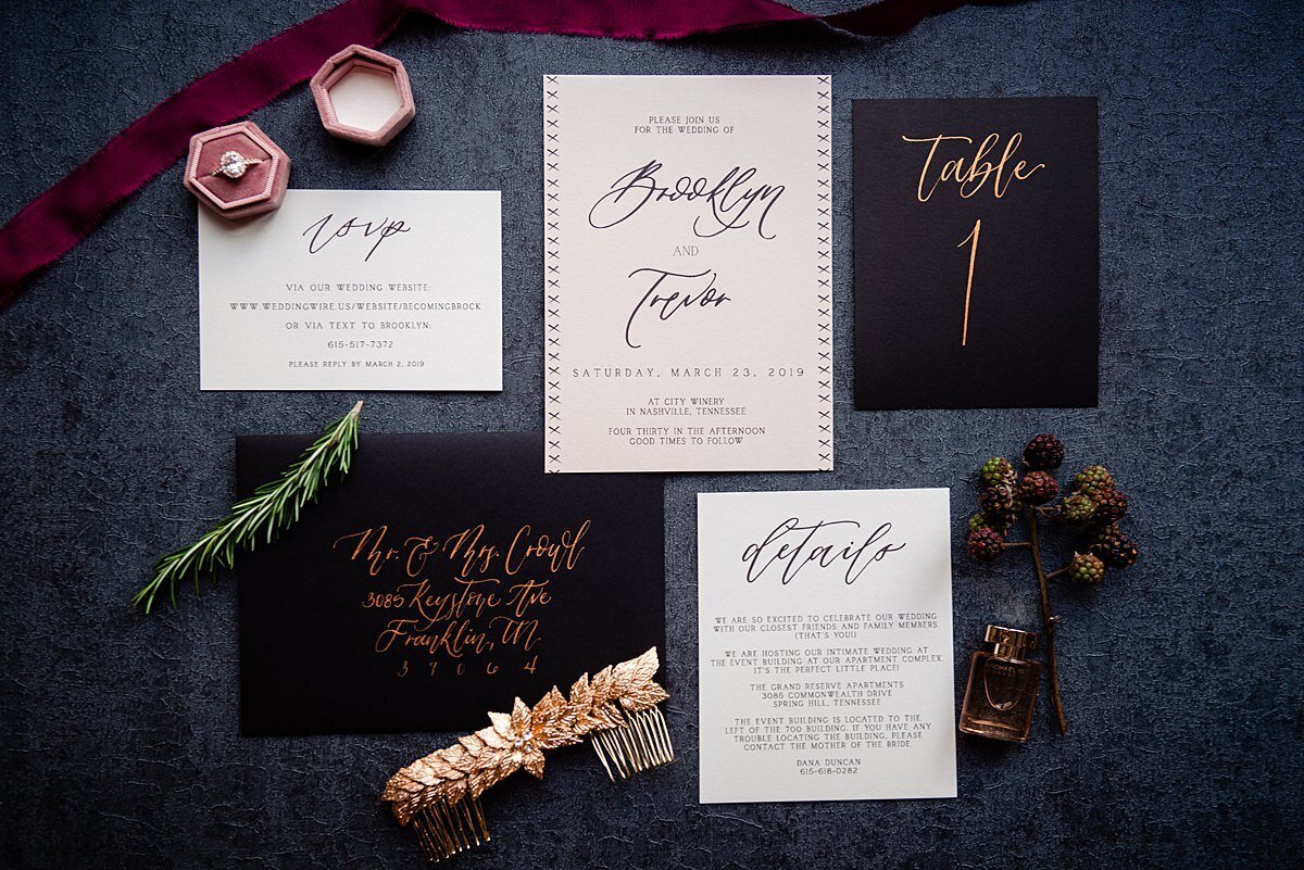 Black and white wedding stationery suite with diamond engagement ring in blush velvet ring box with burgundy ribbon and a gold hair comb on a navy background.