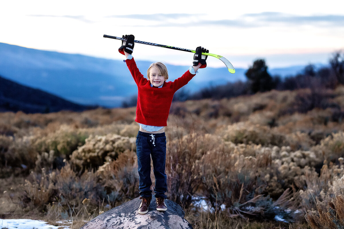 A happy little boy, lifting his hockey stick into the air.
