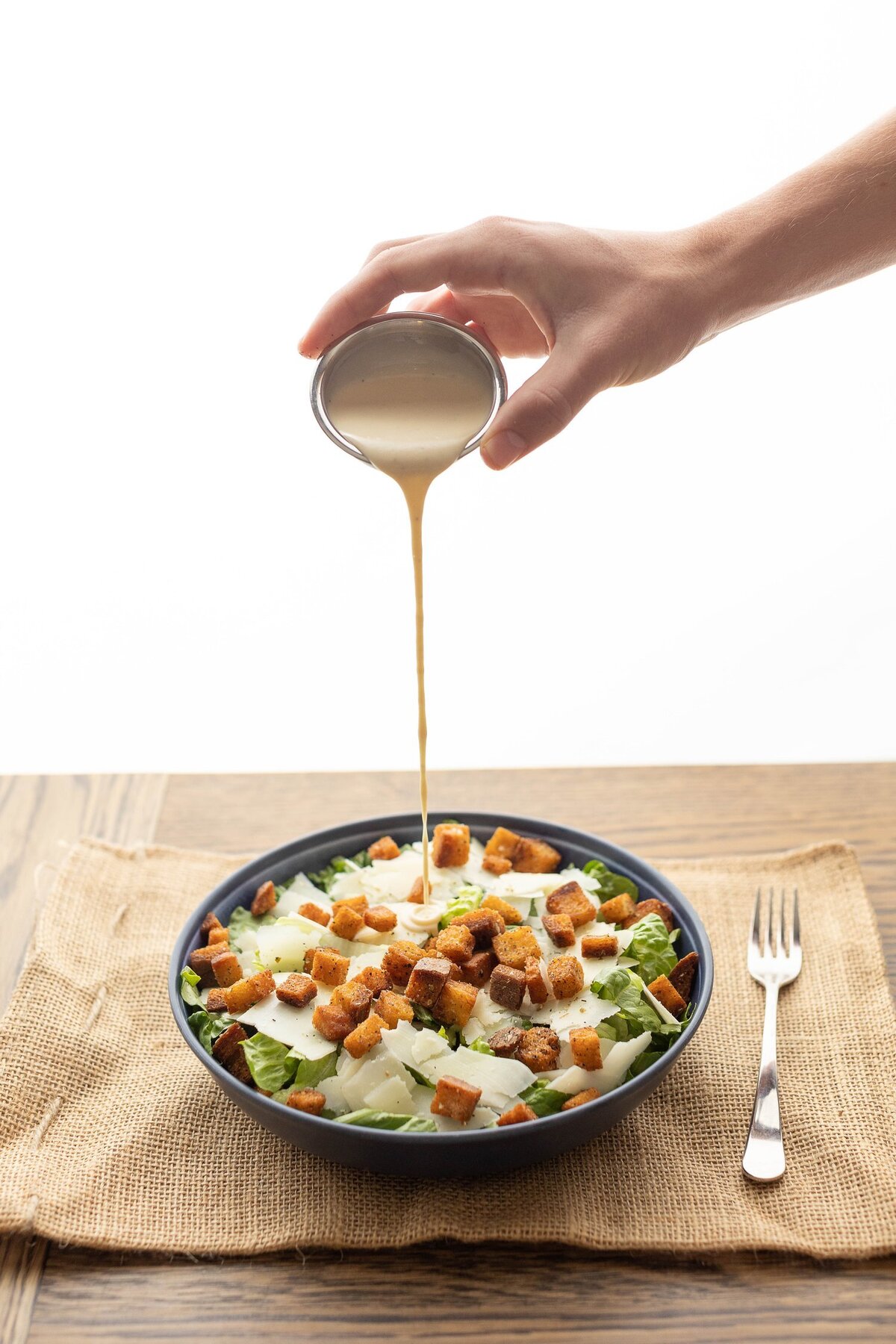 Ceasar Salad with a hand drizzling dressing over it