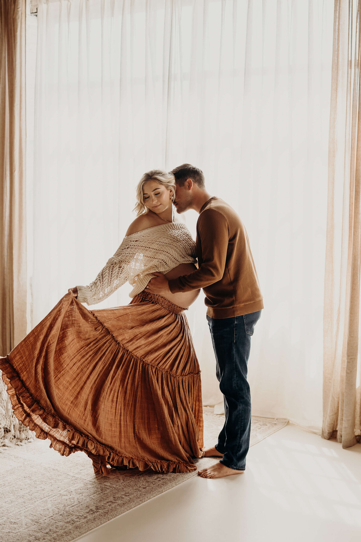 expectant couple embrace in beautiful backlit room