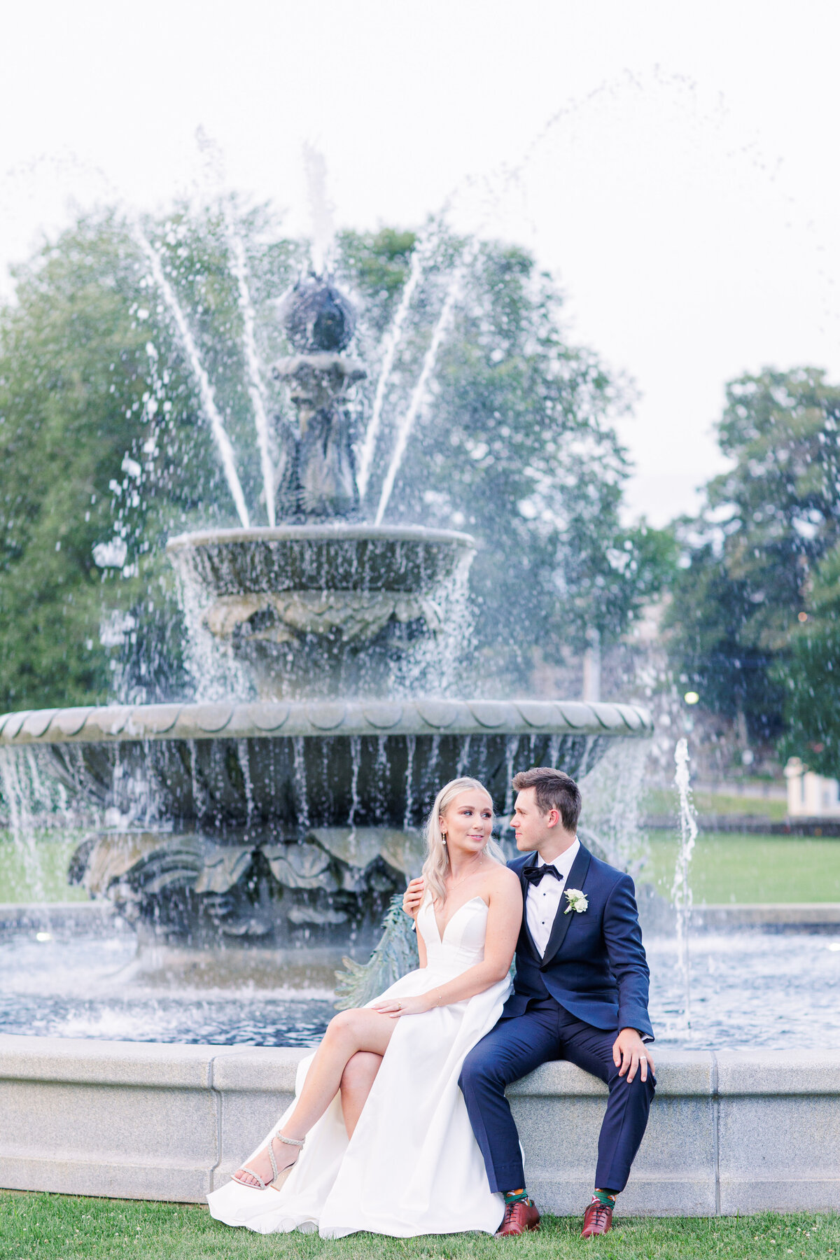 Bride and groom looking at each other while sitting at the fountain outside of Tupper Manor