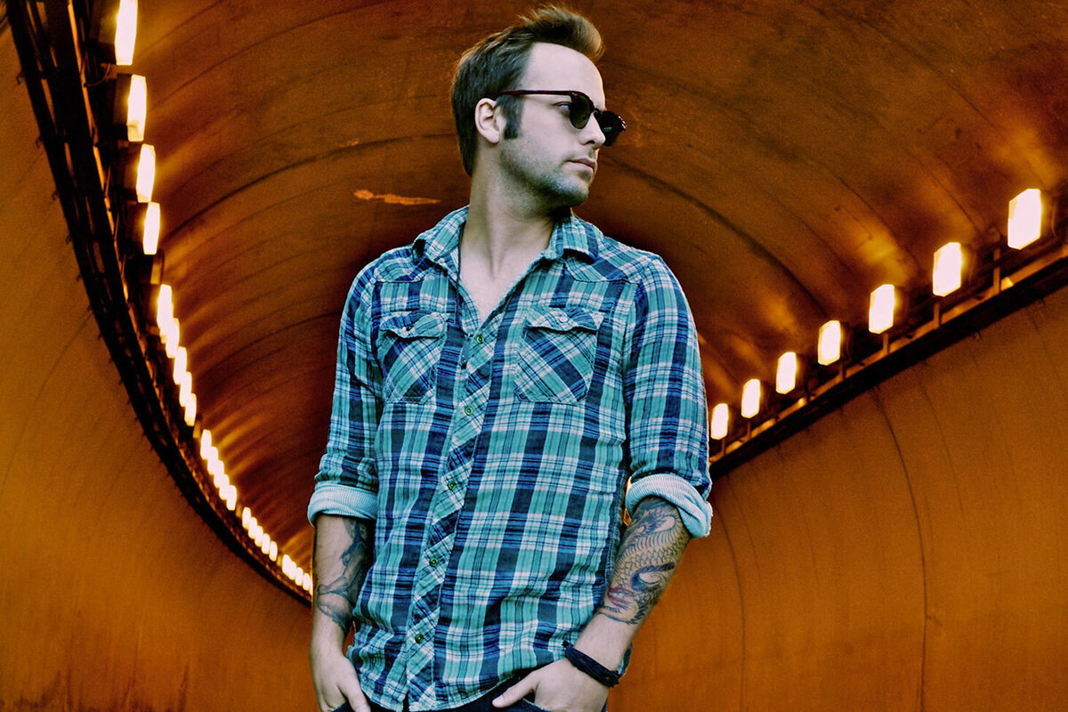 Country Music portrait Dallas Smith standing in lighted tunnel wearing plaid shirt and sunglasses
