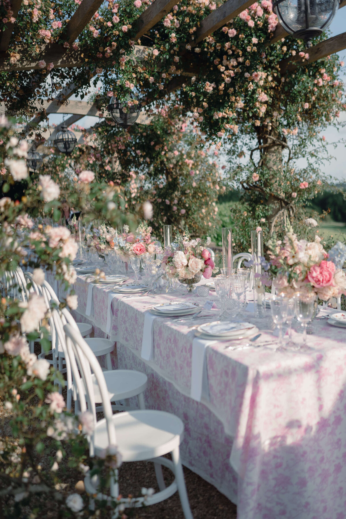 wedding dinner table with pink and white floral linen under a rose arbour full of pink roses in the gardens of the romantic wedding venue euridge manor