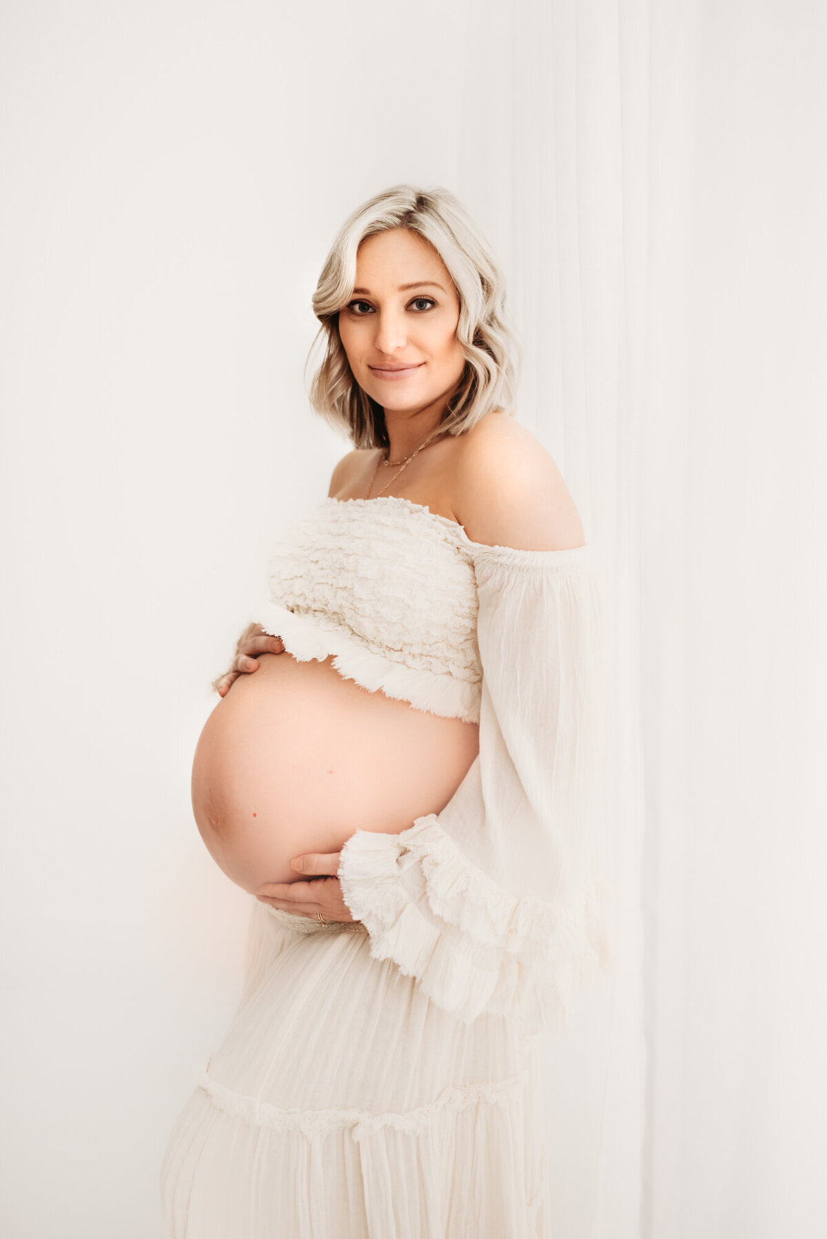 pregnant mother looking at camera holding belly in white room