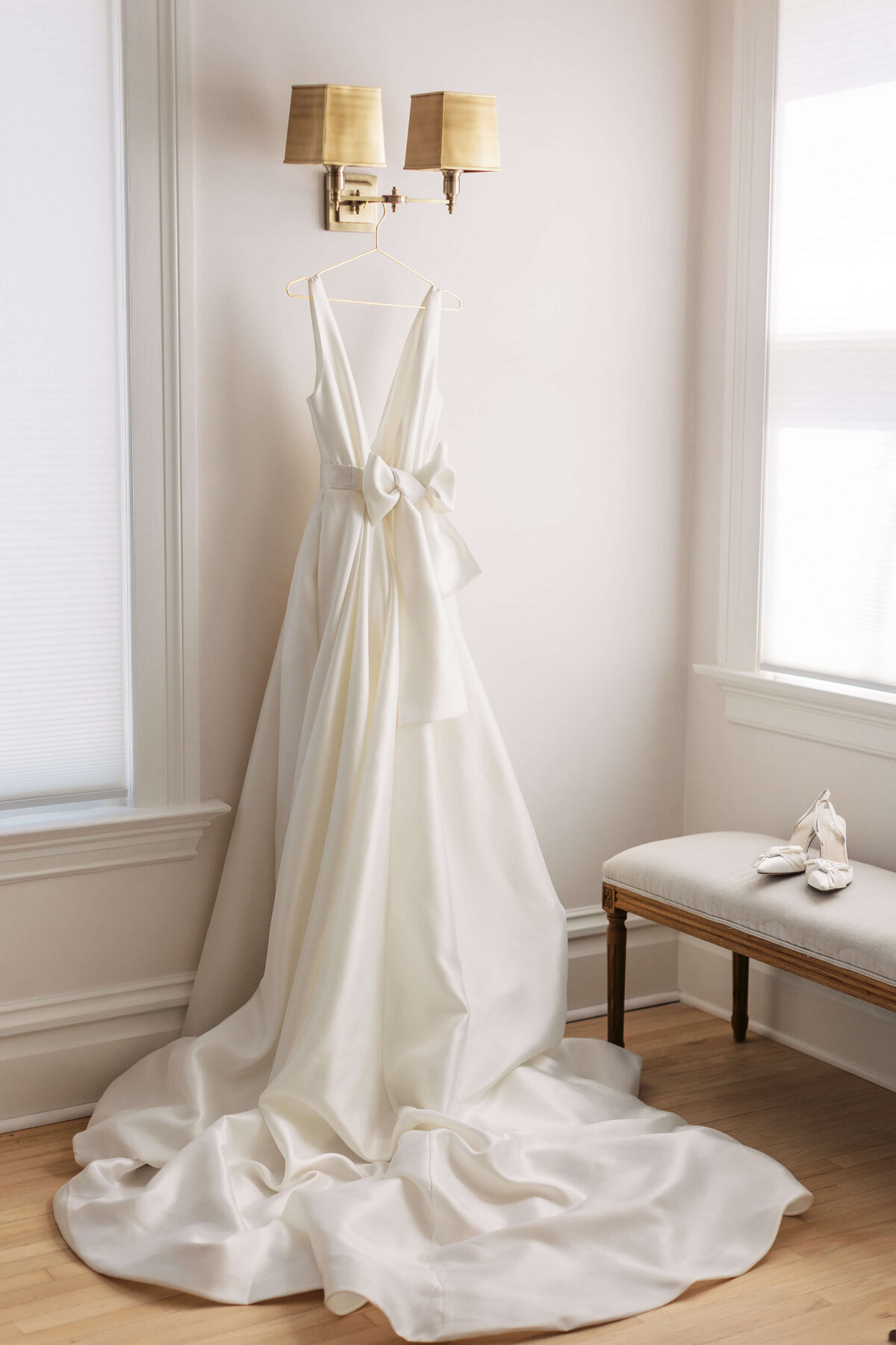 Bridal gown hangs on a light fixture next to bridal shoes.