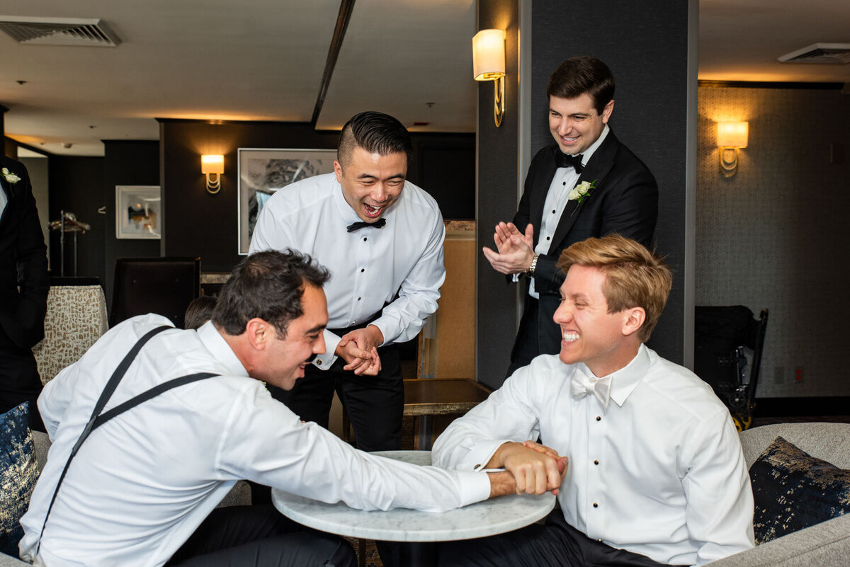 A group of men in tuxedos are sitting around a table laughing