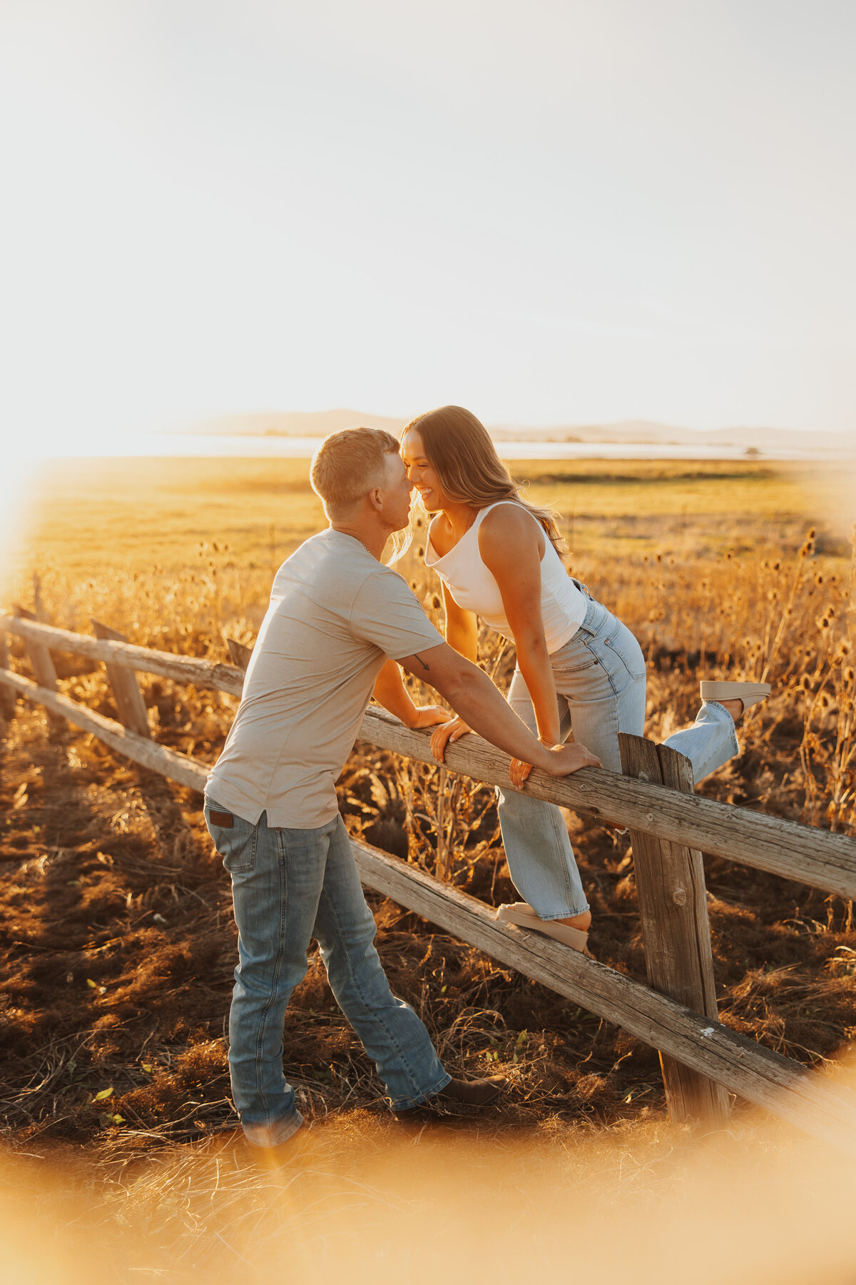 Couple kissing over a rustic fence during golden hour.