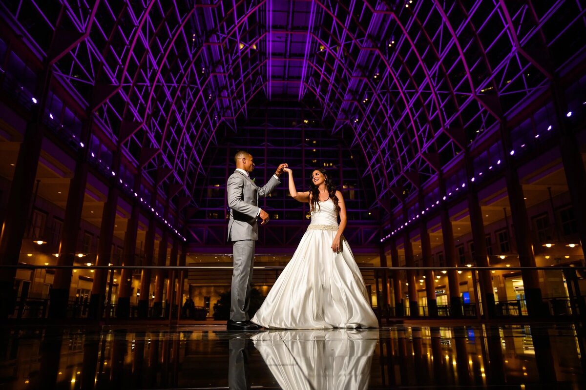 A couple dancing in a grand, illuminated atrium, reflected on the shiny floor, creating a sense of elegance and grandeur.