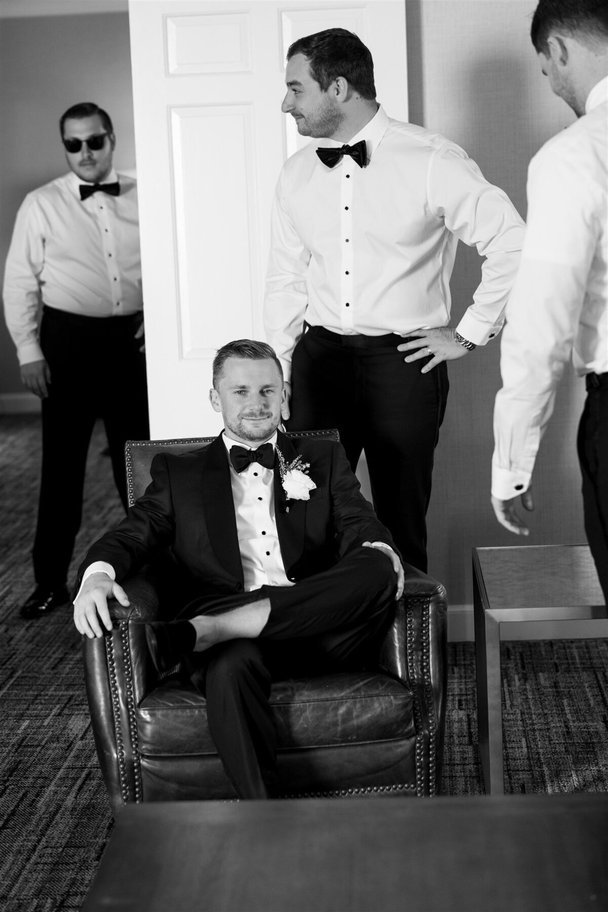 Groom sitting on chair while groomsmen mingle behind him