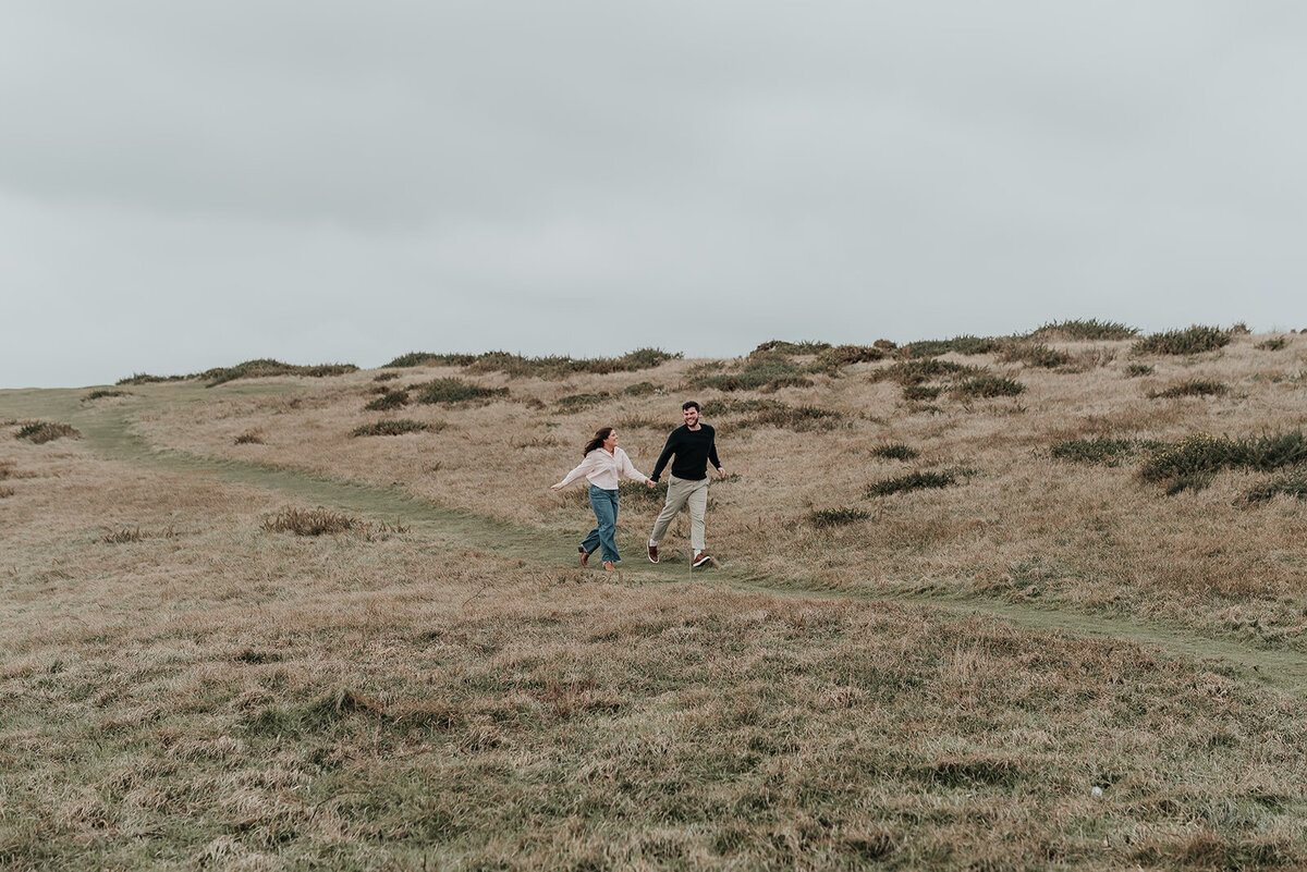 Couple run hand in hand on the downs at Beachy Head Eastbourne