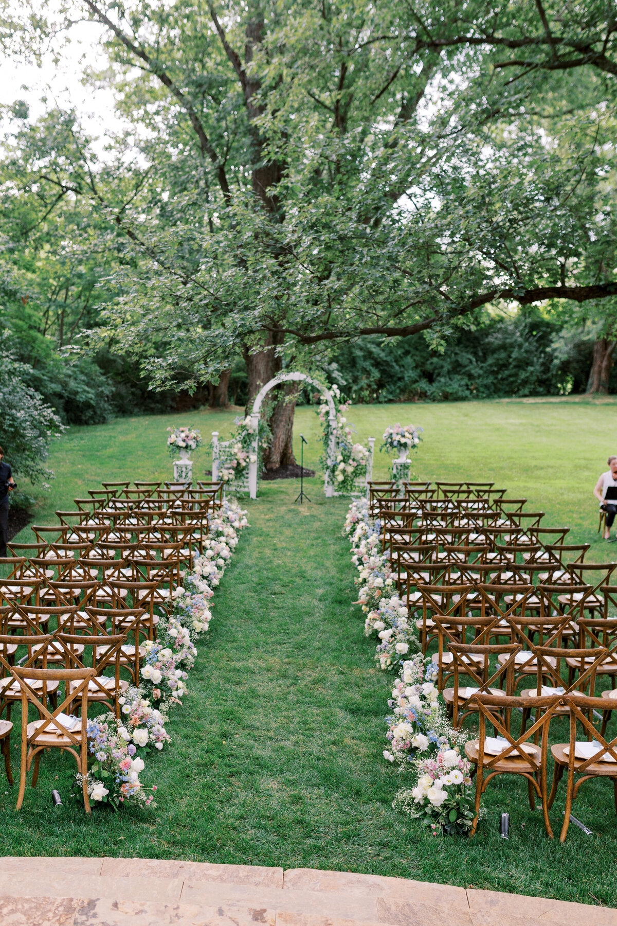 Cross back wooden chairs with a flower lined aisle for a wedding ceremony