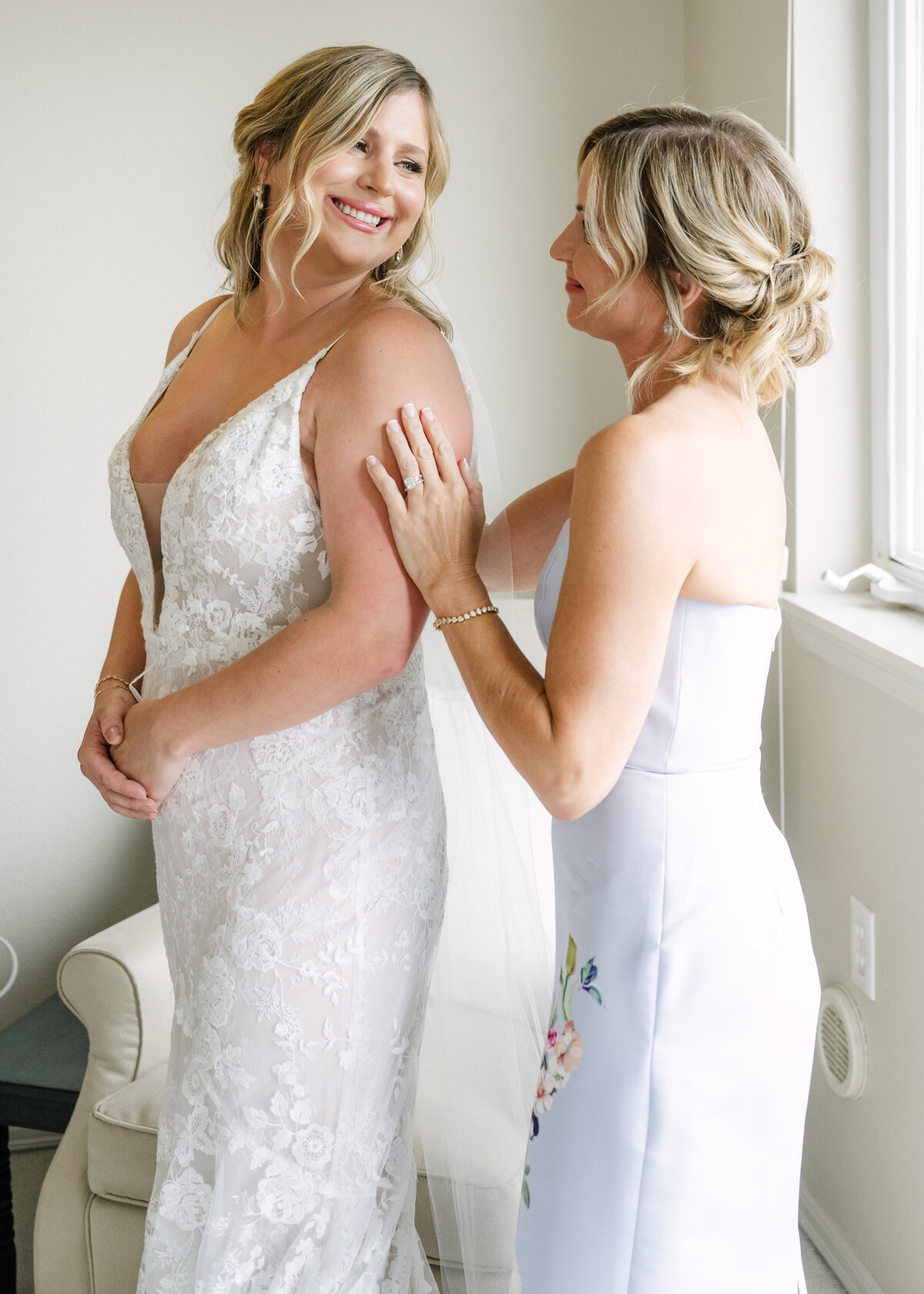 bride and mom prepare for wedding indoors by window