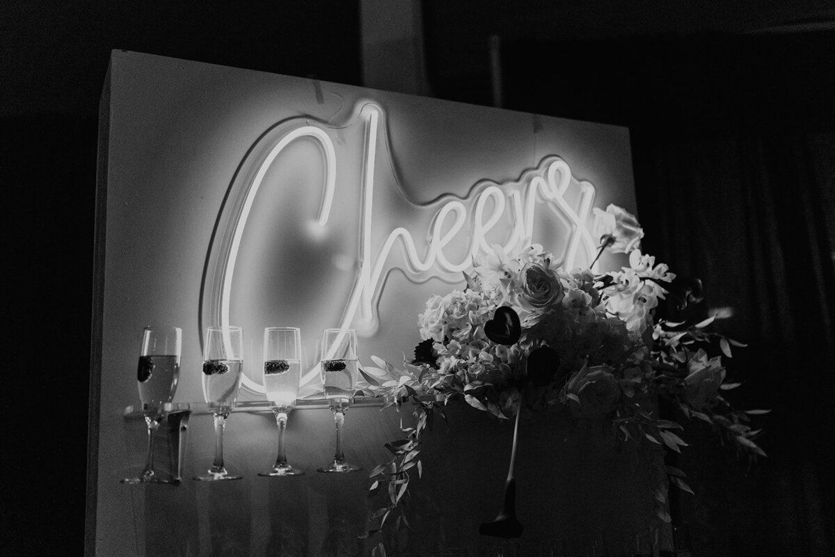 Wedding reception with a champagne wall and neon cheers sign.