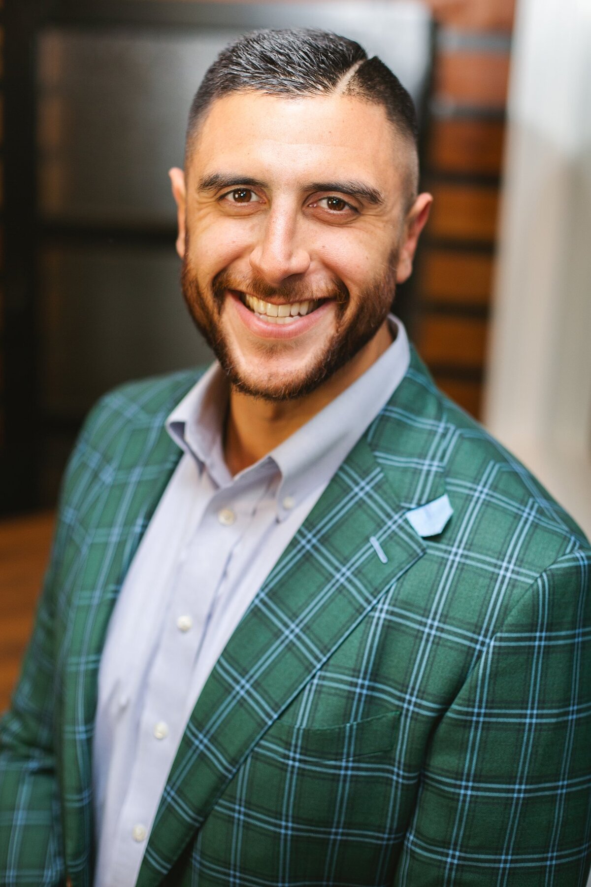 A-smiling-man-in-a-green-plaid-suit-during-a-professional-headshot-session-in-an-industrial-office-space-in-Indianapolis