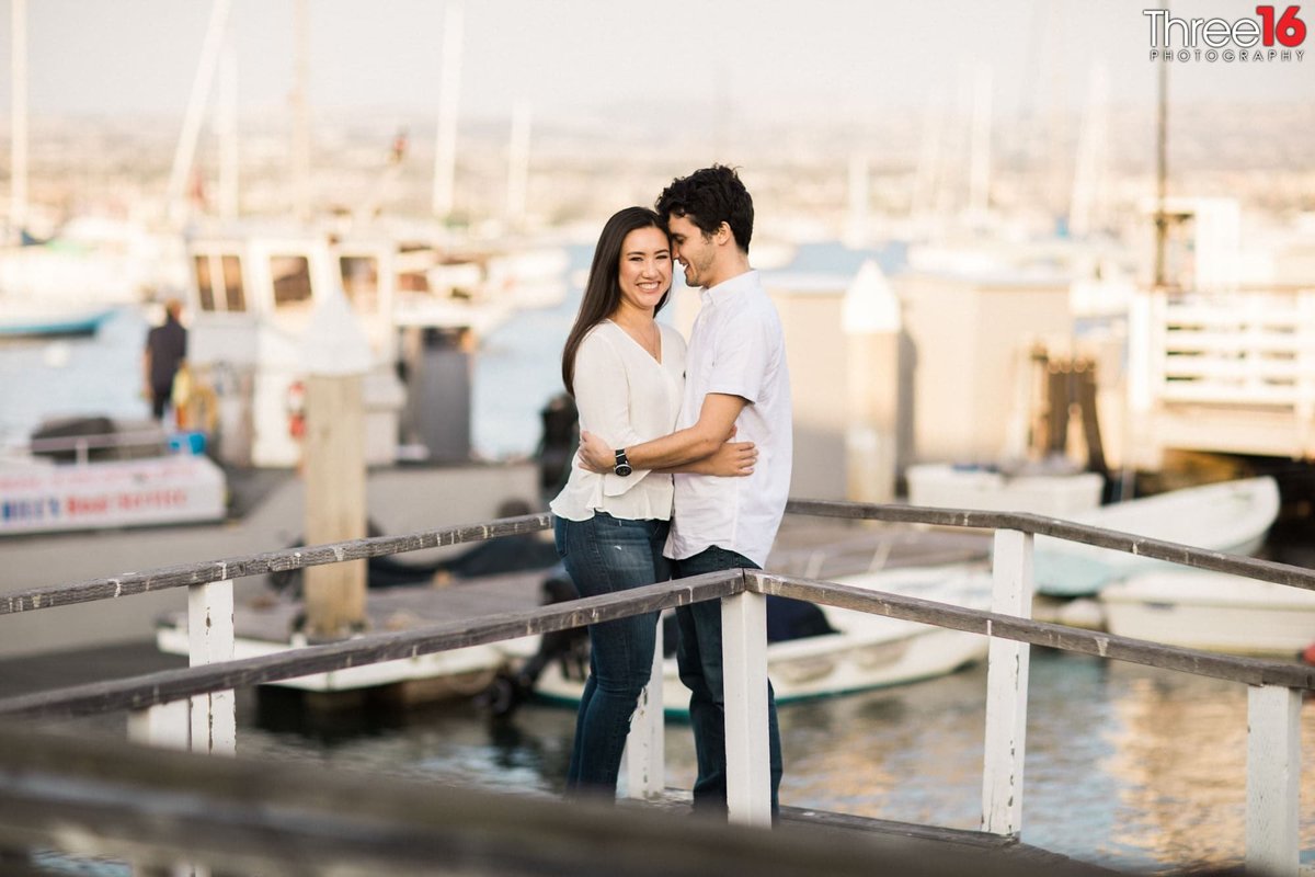 Couple embrace while standing on the harbor dock during engagement session