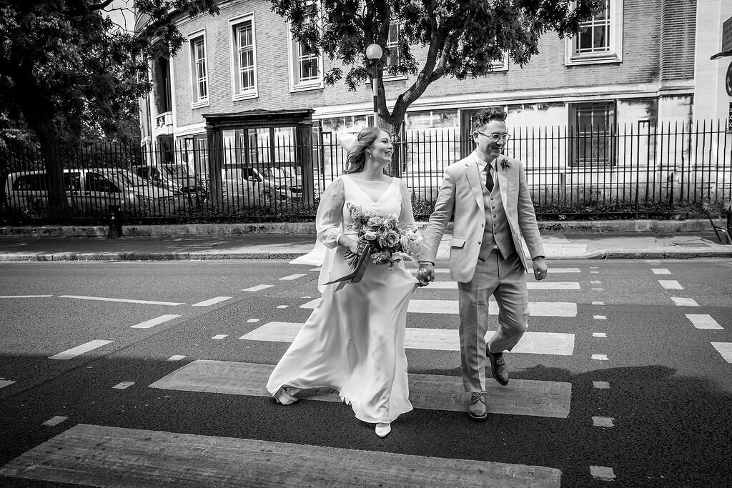 Brides dress blose in the wind ad bride and groom use zebra crossing to cross London street