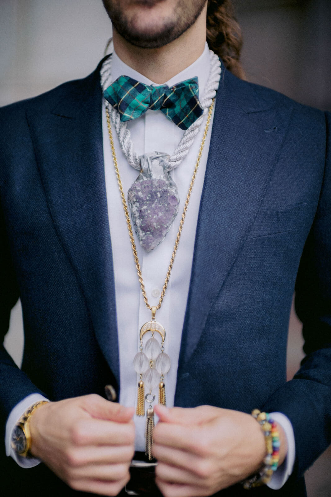 The groom, is wearing a black suit, checkered turquoise bow tie, necklaces, and bracelets in NYC City Hall. Image by Jenny Fu Studio