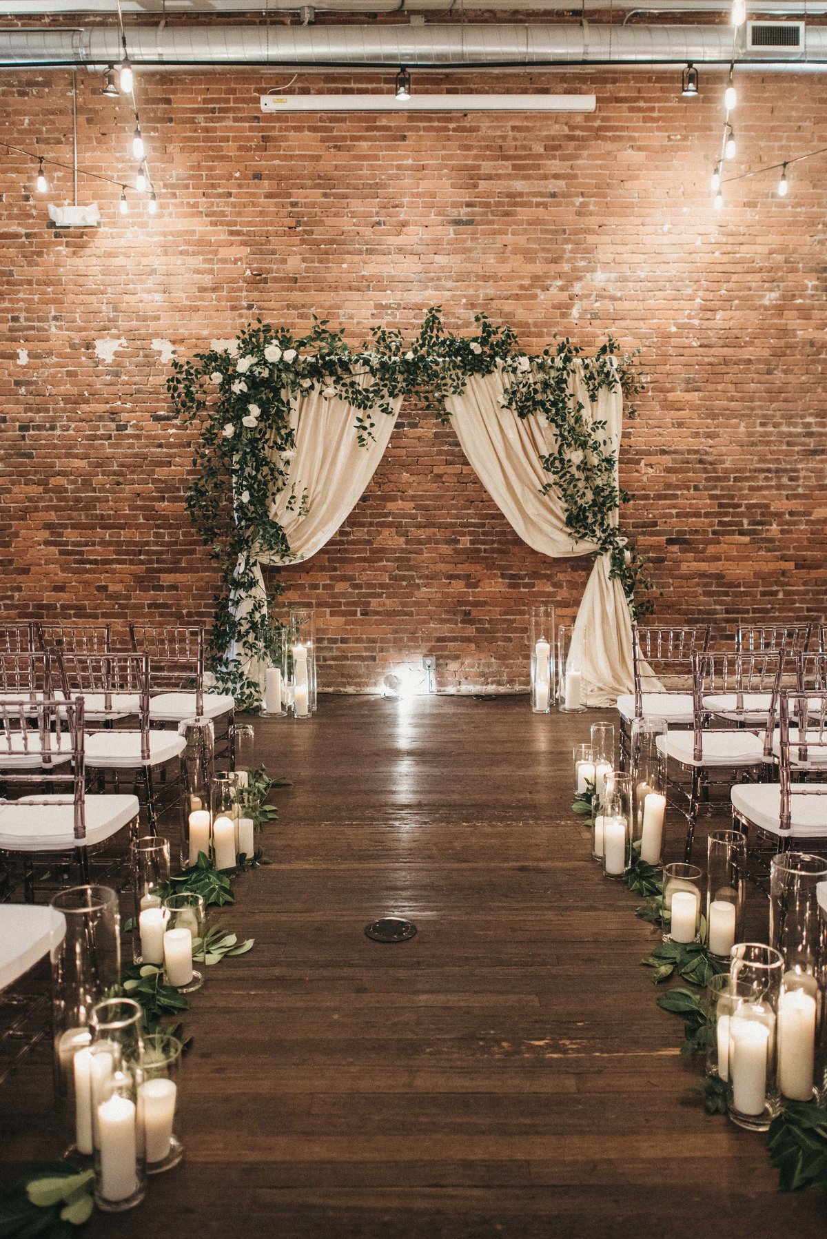 Axis Pioneer wedding with draped wedding arbor covered in greenery and aisle lined in candles and greenery