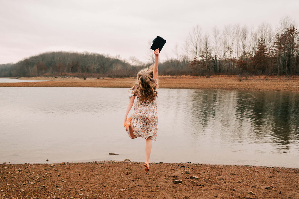 Branson senior photographer Jessica Kennedy of The Xo Photography captures senior girl jumping holding graduation cap near the lake