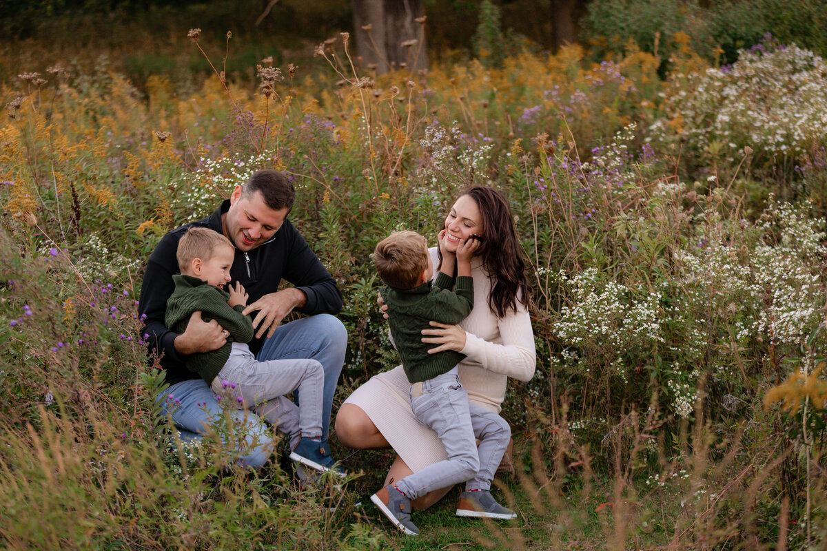 A family  tickles each other in a bed of fall flowers at Mayslake Forest PReserve.