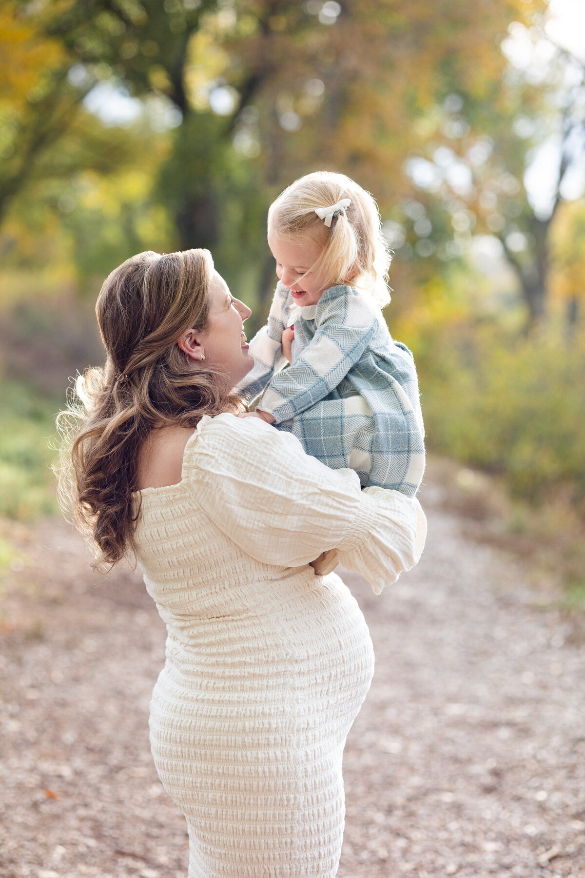 Pregnant mom and toddler daughter smile at each other as mom holds daughter.