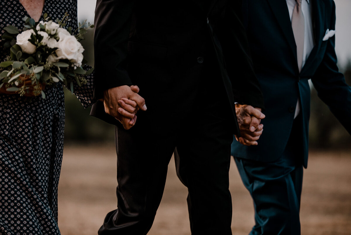 Groom holds his grandparents hands while walking them down the aisle