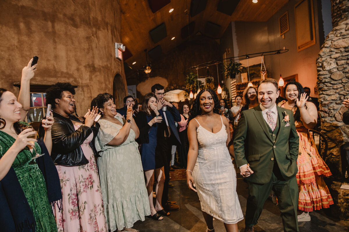 A couple holding hands as they exit their reception with guests cheering 