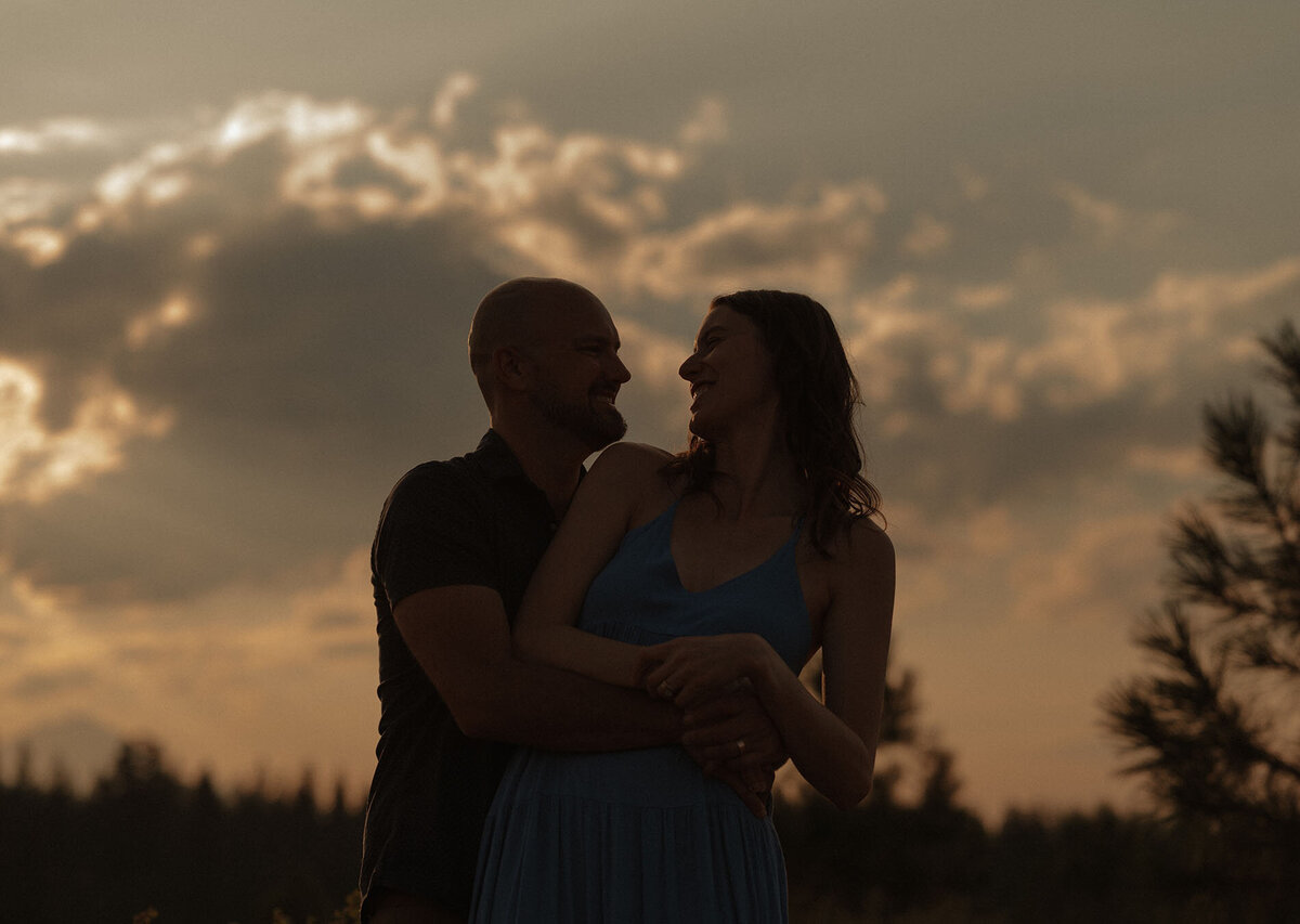 expecting parents embrace while their silhouette stands out against the sky