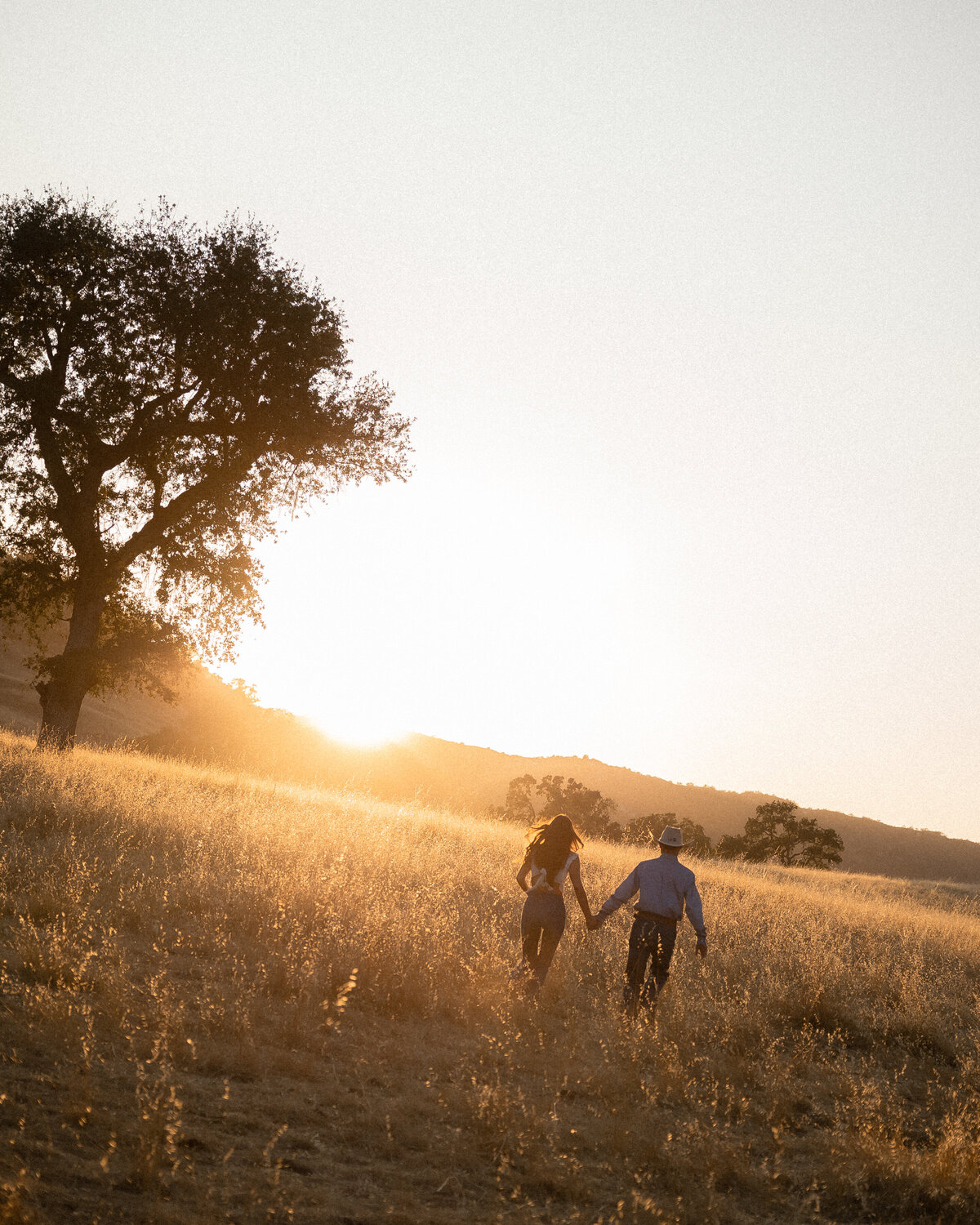 candid couple running during engagement photos in open field during golden hours in San Luis Obispo