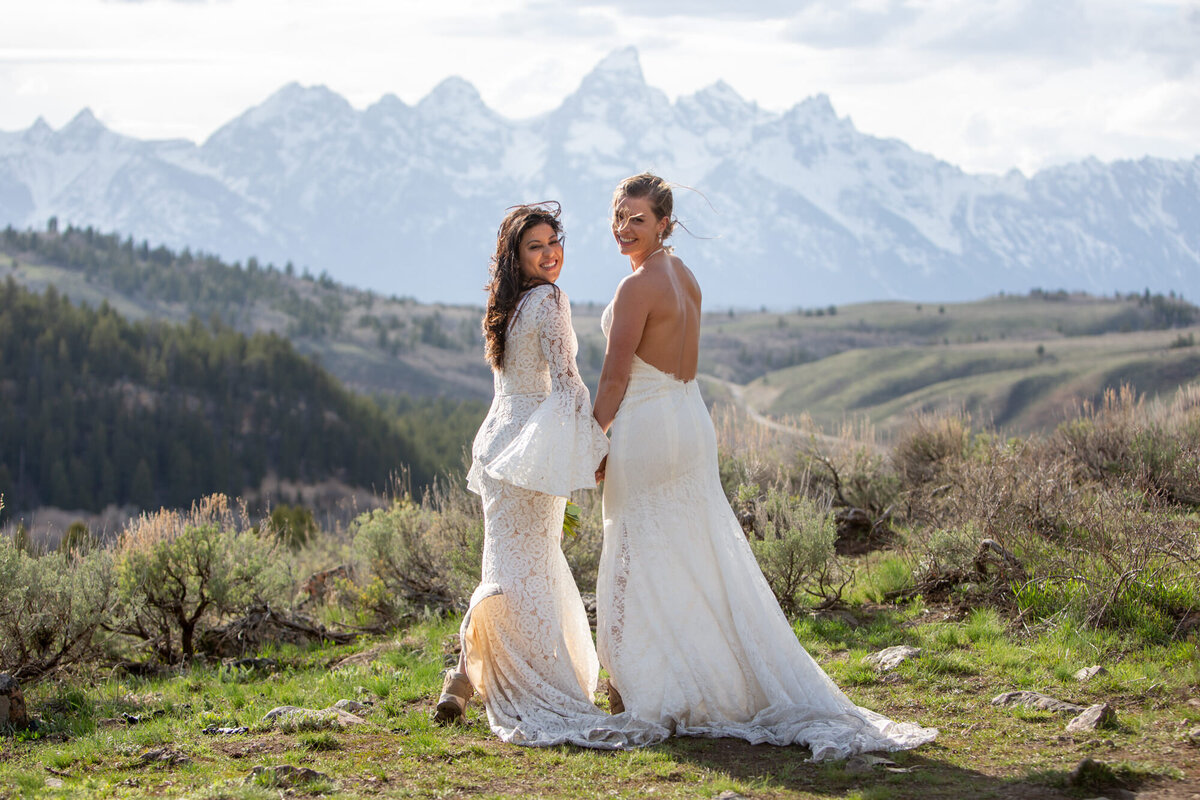 Two brides holding hands smile back at their Wyoming elopement photographer.