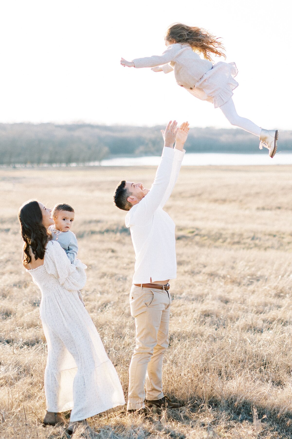 Family of 4 playing in a field at sunset for family photos tossing daughter up in the air