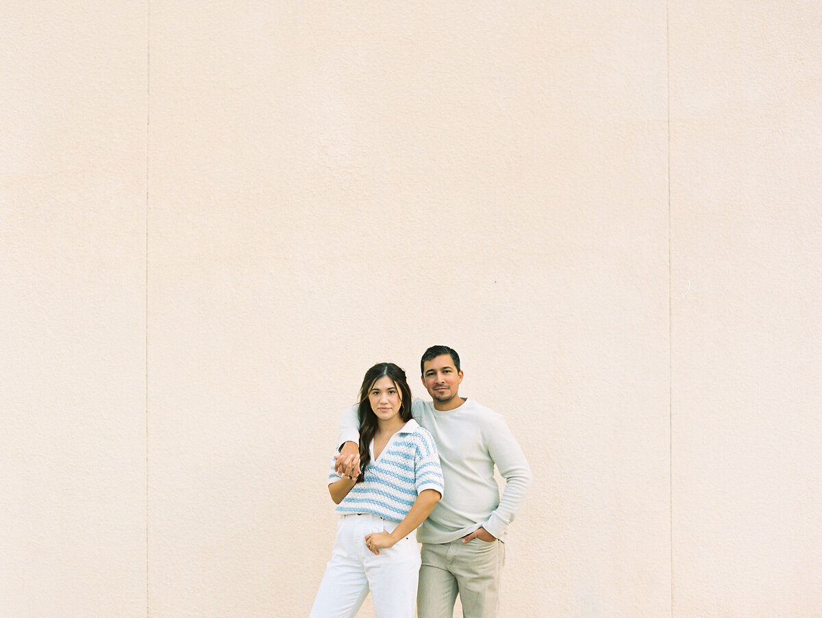 Couple holding hands and posing against a light colored wall