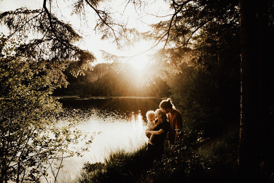 mamma håller barn i famnen och pappan står bakom i en skog i solnedgången i halmstad