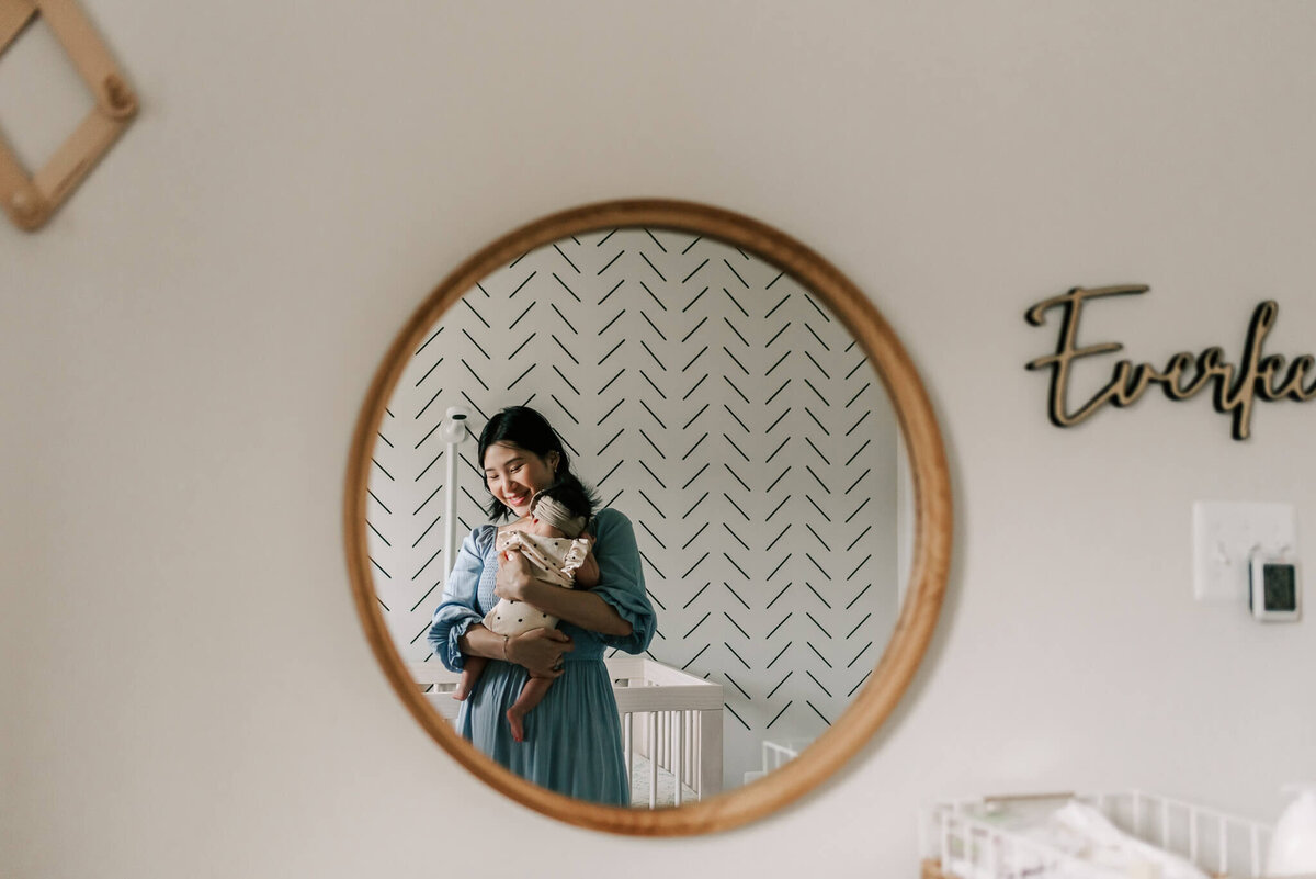 A reflection in a round mirror captured by a northern virginia newborn photographer, of a mother holding her daughter