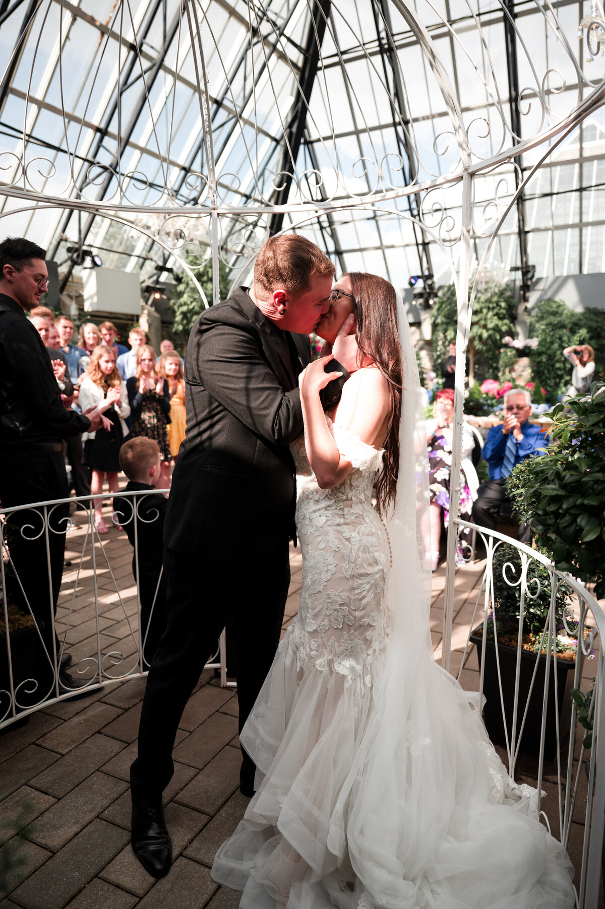 bride and groom first kiss on wedding day with all of their guests cheering behind them