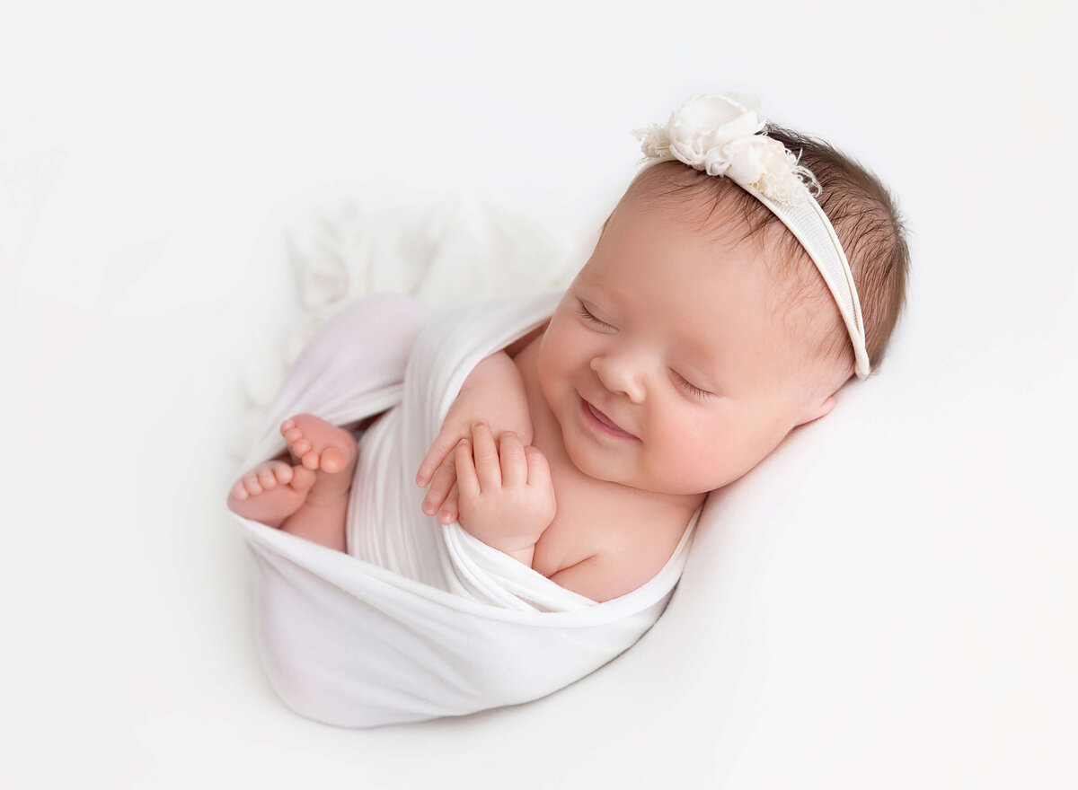 Newborn baby girl smiling on white blanket Rochel Konik photography