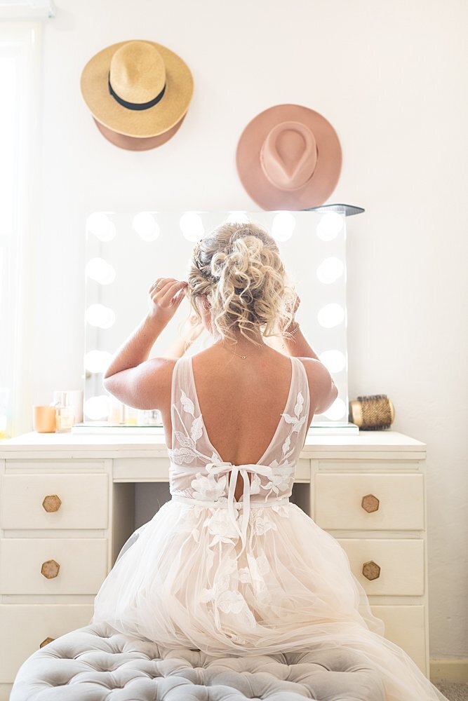 Stylish bride fixing hair in lighted mirror