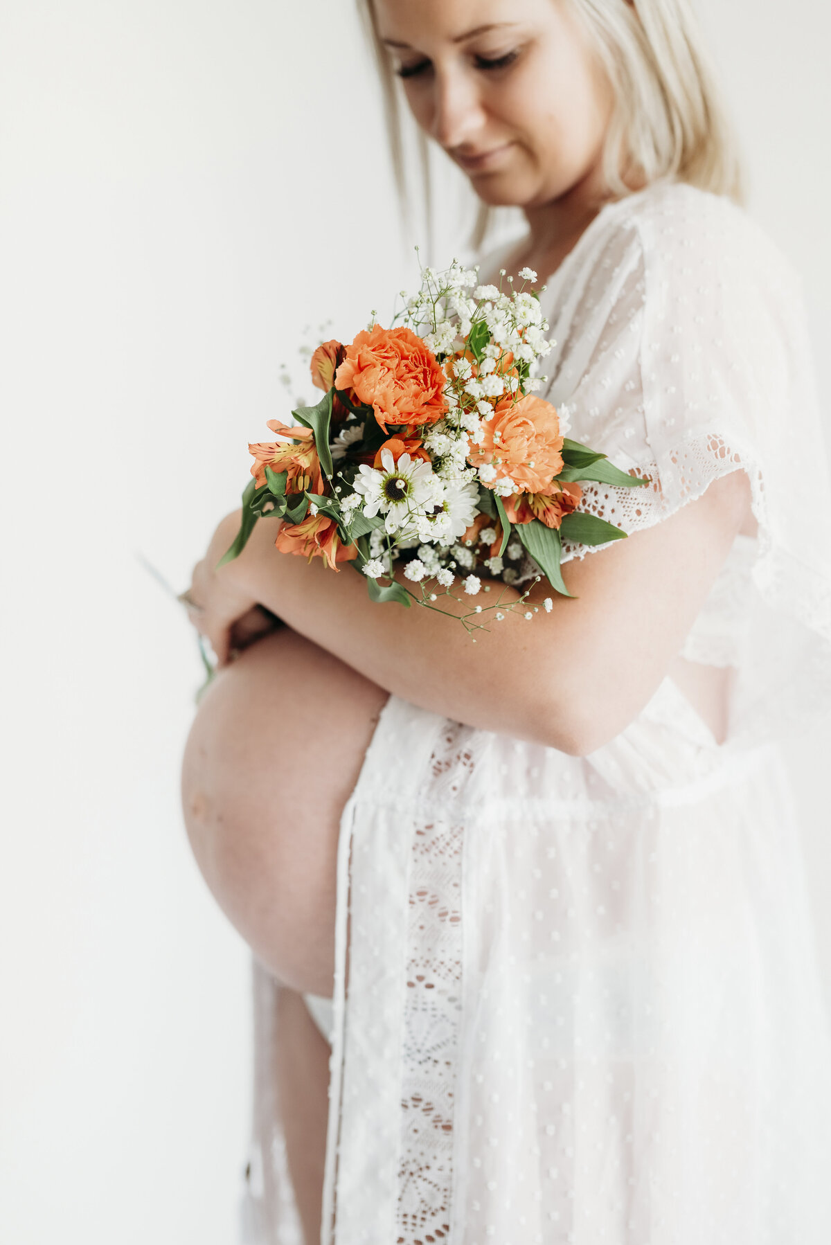 Maternity portrait with bright bouquet held against a white background, highlighting bump and florals.