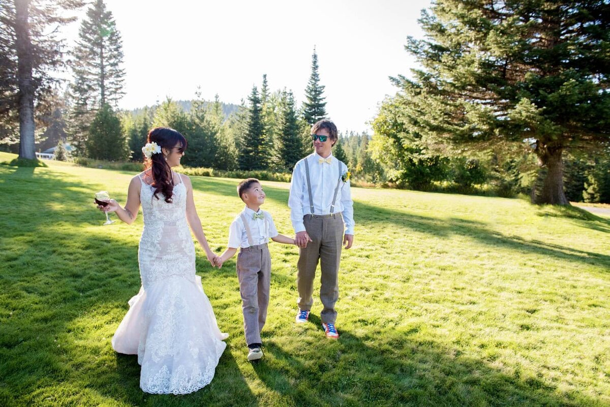 a bride and groom walk through a yard holding hands with a young boy