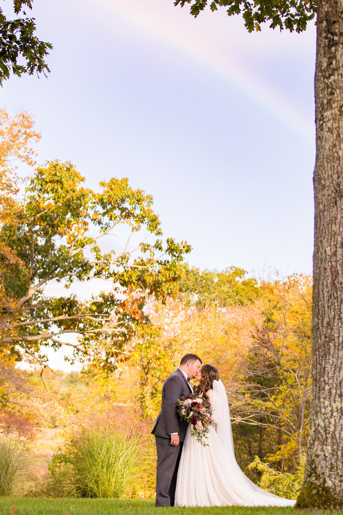 Transgender groom kisses his bride under a rainbow.