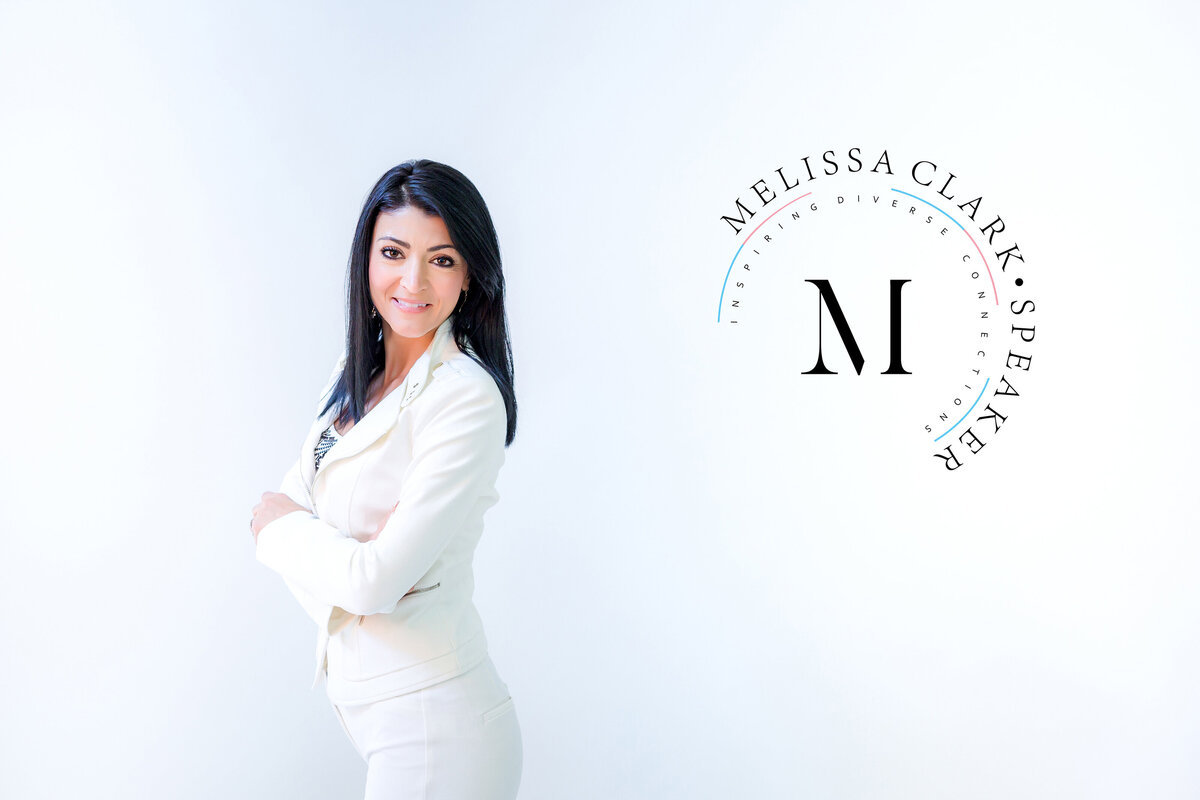 A female speaker wearing a tailored cream suit, standing with arms crossed in front of her business logo and looking at the South Shore MA branding photographer